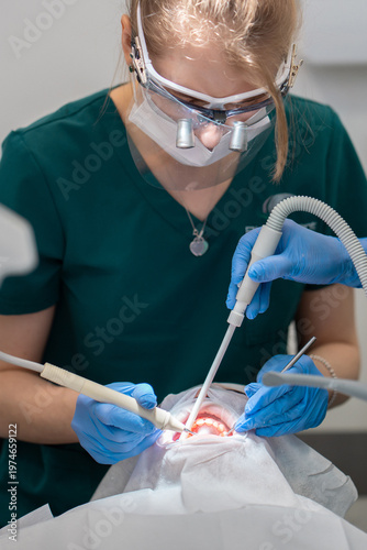 Dental hygienist performing scale and polish treatment for patient. Specialist using ultrasonic scaler and suction tool for plaque removal and oral hygiene service in clinic.