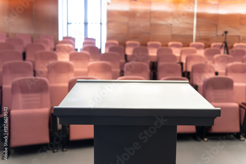 Tableau sur toile Empty lecture hall with podium in foreground and rows of pink seats under soft w
