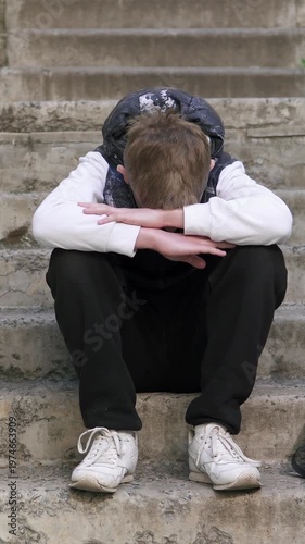 Sad teenage boy sitting outdoors after school, feeling lonely and thoughtful. The concept of school bullying. Vertical video.