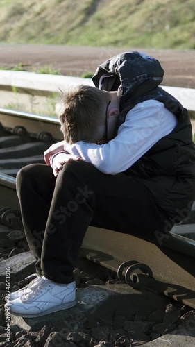 A young man in glasses sits sadly on a railway track, symbolizing loneliness and despair. The scene reflects the emotional impact of school bullying.