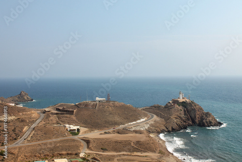 A stunning view of the 1863 lighthouse in Cabo de Gata, Andalusia, constructed upon the historic ruins of the San Francisco de Paula castle. The white beacon stands prominently on a volcanic cliff