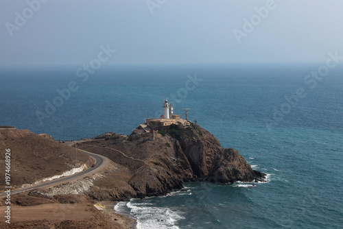 A majestic view of the Faro de Cabo de Gata, built in 1863, perched on a fifty meter high volcanic cliff. The lighthouse stands as a landmark against the deep blue Mediterranean water, Almeria region