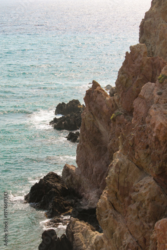 A dramatic coastal shot of ancient, weathered rocks protruding from the crystal-clear blue waters of the Mediterranean Sea. Located in the Cabo de Gata-Nijar Natural Park in Andalusia
