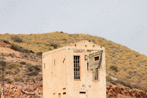 A low angle shot focusing on the crumbling upper architectural details of a derelict mining building in Cabo de Gata Natural Park. The industrial rooftop stand out against a cloudy sky
