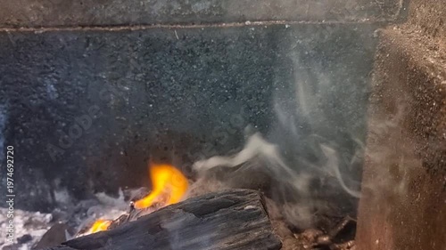 Close-up of burning logs and smoke in a fireplace