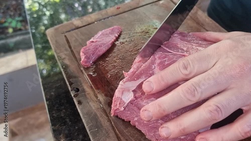Hands slicing raw red meat on a wooden cutting board