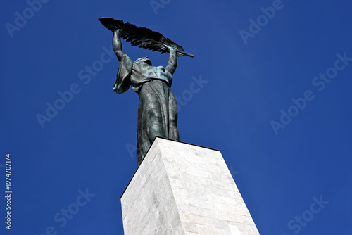 the newly refurbished Statue of Liberty on top of the Gellert hill. bronze woman's figure with palm lea. opened to tourist and locals on April 5 2026. stone base. blue sky. low angle perspective view