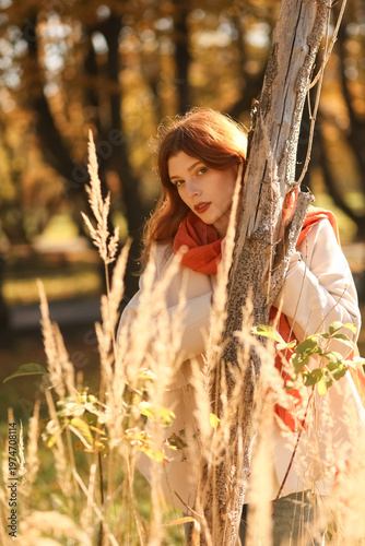 Red-haired woman in autumn park wearing coat, jeans and scarf