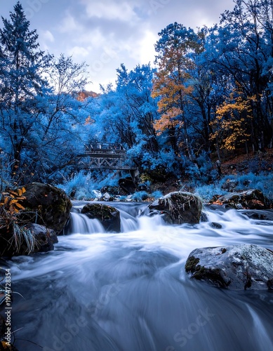 A serene river flows through a vibrant forest with hints of autumn foliage. A small bridge spans the water's path
