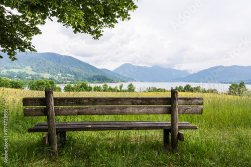Empty wooden bench on a green meadow with a scenic view of Tegernsee lake and Alps

