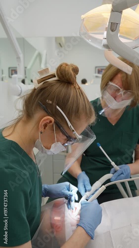 Female specialist uses ultrasonic device to clean patient tooth surface from hard calculus deposits in clinic. Dental team works together providing hygienic periodontics care and therapy