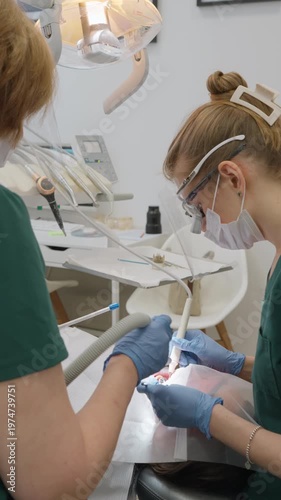 Specialist uses vibrating ultrasound scaler to remove stubborn tartar from patient mouth. Assistant manages suction process. Clinical hygiene procedure ensures optimal stomatology health