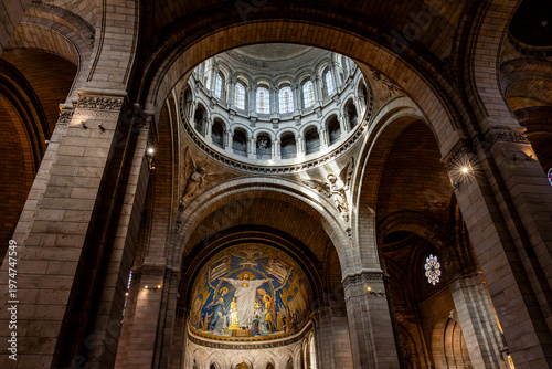Interior view of the Basilica of the Sacred Heart of Montmartre showing the central dome with mosaics, the nave and colored stained glass windows in warm light, in Paris, France.