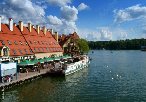 Foto View of the Mikolajki harbor promenade with historical buildings and a cruise ship docked at the pier