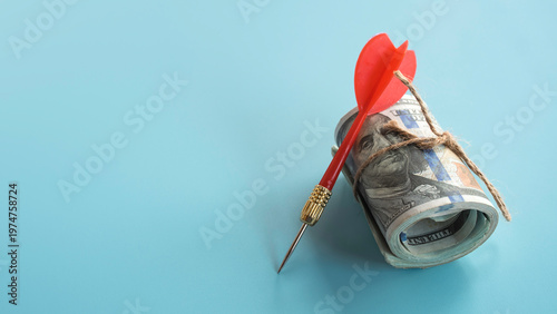 Tableau sur toile Red dart leaning against a roll of US dollar bills for financial targeting