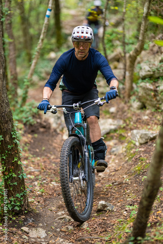 Man mountain biking on a narrow forest trail wearing helmet and protective gear during a summer ride