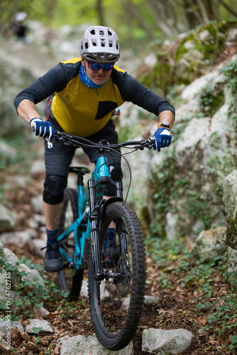 Experienced mountain biker rides a teal full-suspension bike on a rocky forest trail