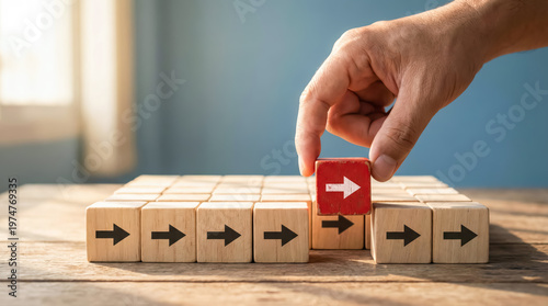 Hand placing a red wooden block with an arrow pointing in the same direction as other blocks on a wooden table
