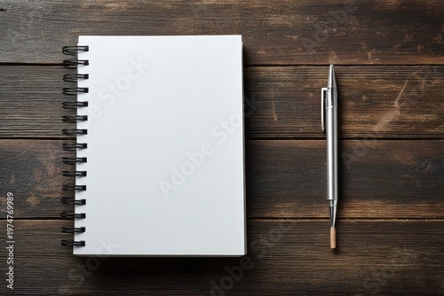 Top view of blank spiral notebook and silver pen on weathered dark wooden table surface with textured grain natural light creating a simple and clean composition for writing or sketching