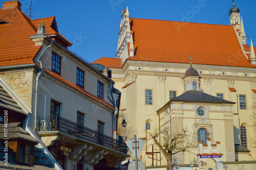 Historic Renaissance buildings and the Parish Church with red tiled roofs under a clear blue sky in the charming old town of Kazimierz Dolny, Poland during a sunny day.