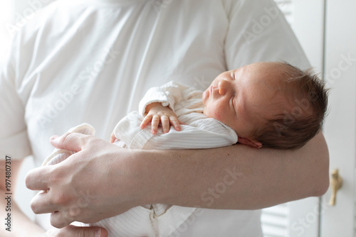 Wallpaper Mural Close-up of a newborn baby sleeping peacefully in the arms of a parent wearing a white shirt. The tender moment, soft natural light, and gentle pose convey warmth, safety, and family bonding. Torontodigital.ca