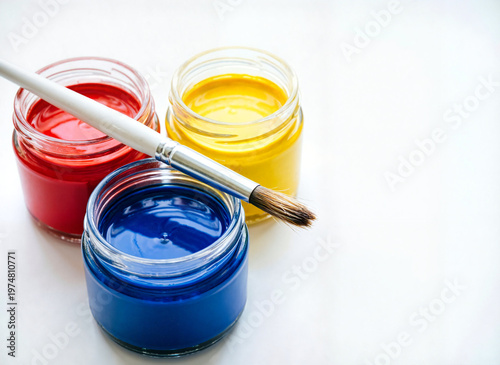 glass jars containing acrylic paint with paintbrush on white