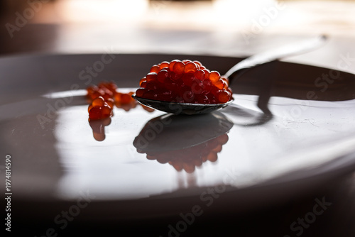 Photos A spoonful of red caviar lives on a plate. Creates a shadow.