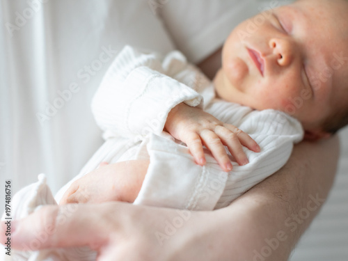 Wallpaper Mural Close-up of a newborn baby sleeping peacefully in the arms of a parent wearing a white shirt. The tender moment, soft natural light, and gentle pose convey warmth, safety, and family bonding. Torontodigital.ca