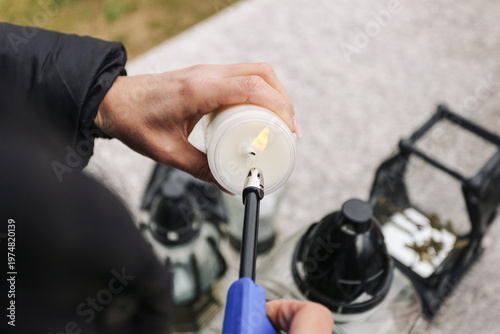Canvas Print Hand lighting candle with long lighter at memorial place surrounded by lanterns