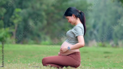 Happy pregnant woman kneeling on green grass in outdoor nature park touching bare belly to relax feeling joyful expectant mother enjoying peaceful maternity care waiting for new baby