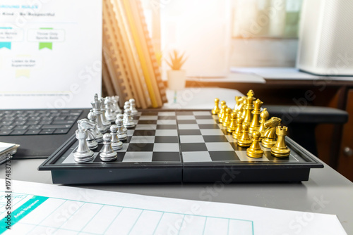Gold and silver chess pieces on a board in an office setting, representing business strategy, competition, and leadership.