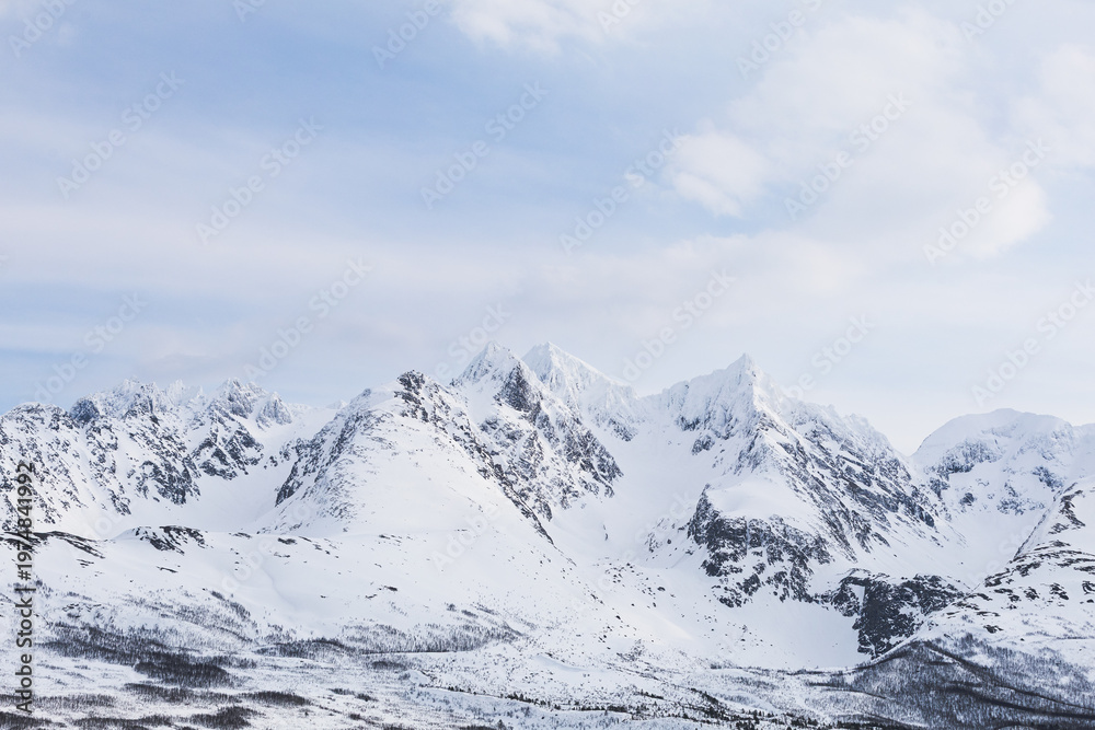 Obraz premium Snow-covered peaks of the Lyngen Alps in northern Norway under clear Arctic sky. Dramatic alpine terrain with rugged ridges and untouched winter landscape