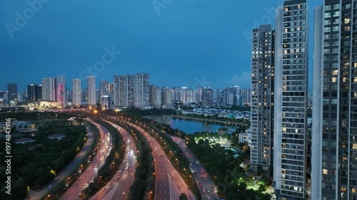 Close aerial view of high rise residential buildings beside Thang Long Boulevard with flowing traffic and lakeside urban scenery during early evening in Hanoi