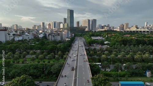 Closer aerial perspective of elevated road in Hanoi showing active traffic flow, surrounding greenery, and dense urban housing with skyline in background