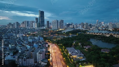Aerial perspective of urban road leading toward modern skyline near lake in Me Tri Hanoi with glowing streetlight and evening city activity