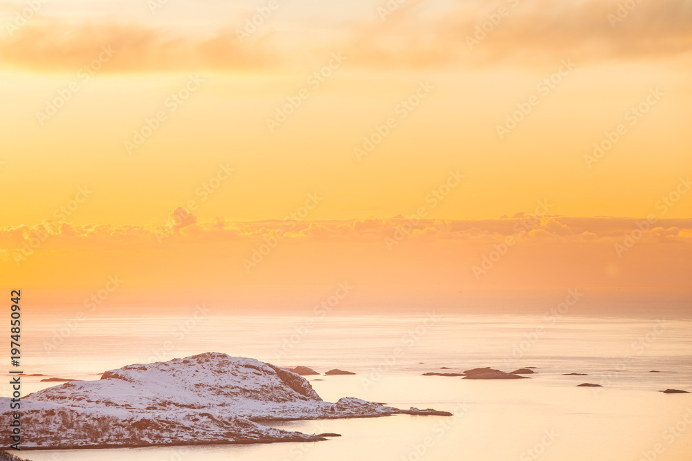 Naklejka premium Golden sunset over a fjord on Kvaloya, Norway, with sun rays spreading above snow-covered mountains