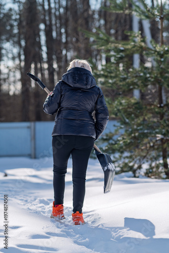 A woman with a shovel walks through the snow.