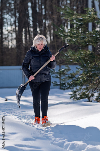 A woman walks through the snow with a shovel in her hands.