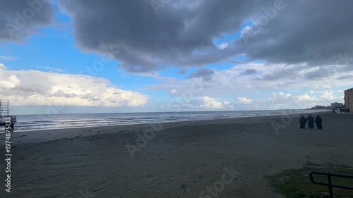 Winter Island. Cloudy coastline, cold sea, sunset, people on the beach. Finikoudes Beach. Larnaca, Cyprus