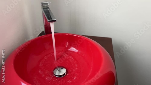 Bathroom red sink, faucet with running water. Saving resources, utility bills. Water resources, water cost