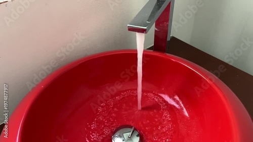 Bathroom red sink, faucet with running water. Saving resources, utility bills. Water resources, water cost