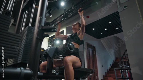 Athletic woman training her back muscles on a lat pulldown machine in a modern gym. She performs a controlled strength exercise targeting the upper back, shoulders, and arms, focusing on proper form