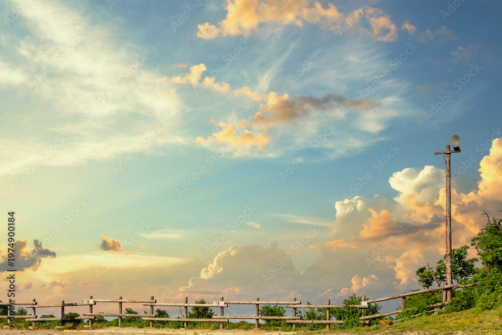Naklejka premium Golden sunset sky with clouds and rustic fence in a peaceful countryside creating a warm natural landscape background with copy space