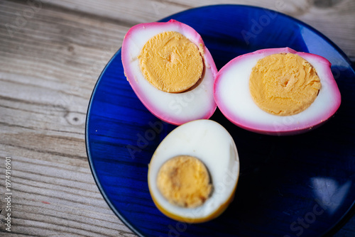 Close-up of halved pickled eggs with vibrant pink and yellow whites on a dark blue plate, showing firm yolks and shallow depth of field. Soft background blur.