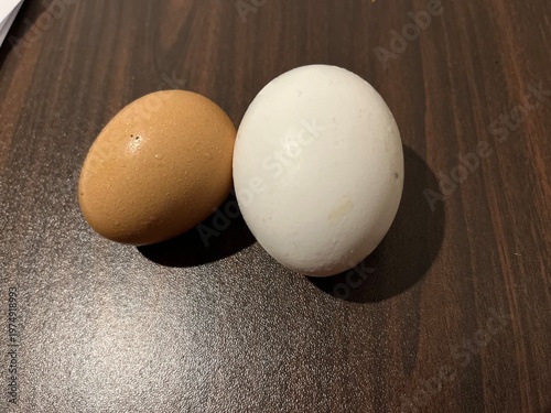 Comparison of natural farm fresh brown egg and industrially produced perfect white egg on dark wood contrast