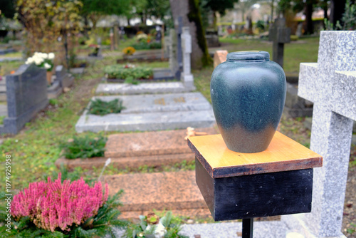A cremation urn rests on a wooden pedestal surrounded by gravestones in a cemetery. Geneva. Switzerland.