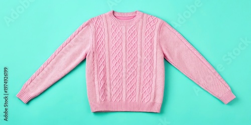 A pink sweater is laid flat on a turquoise background. The sweater features a knit pattern with cables. It is designed for casual wear and comfort. Perfect choice for cool weather