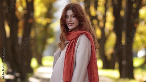Red-haired woman in autumn park wearing coat, jeans and scarf
