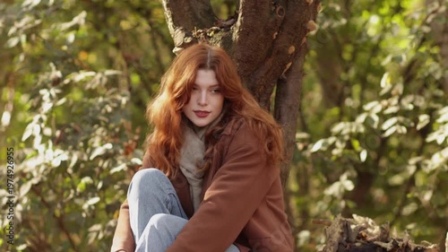 Red-haired woman in autumn park wearing coat, jeans and scarf