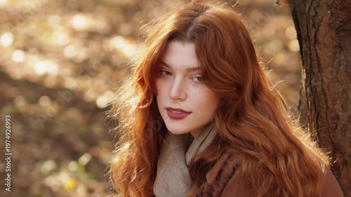 Red-haired woman in autumn park wearing coat, jeans and scarf